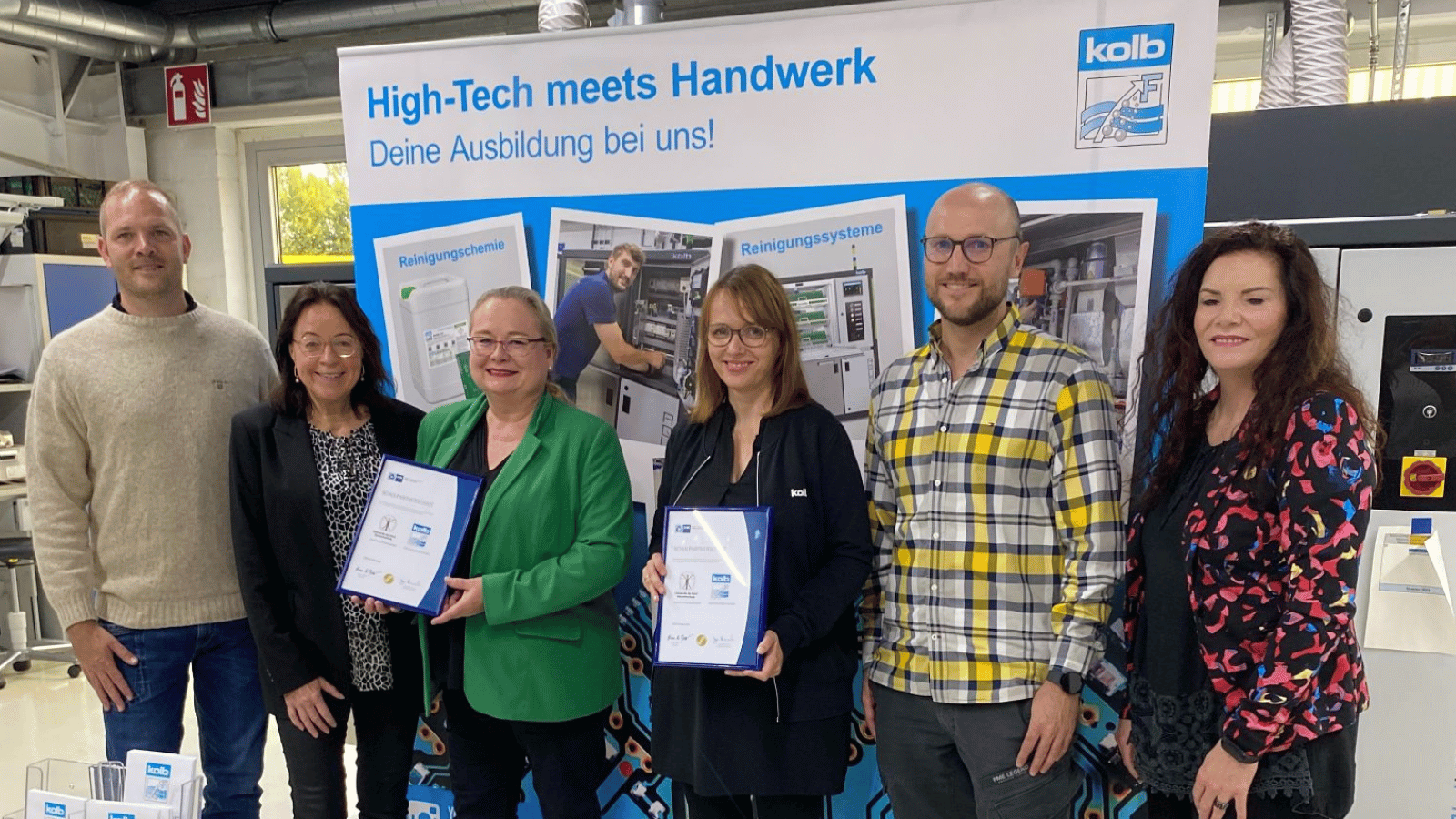 Four representatives of the school with Christin Loekes and Christian Ortmann in front of a Roll up to promote kolbs trainee programme